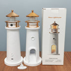 Two white lighthouse-shaped lamps with gold accents, packaging, and accessories on a wooden surface.